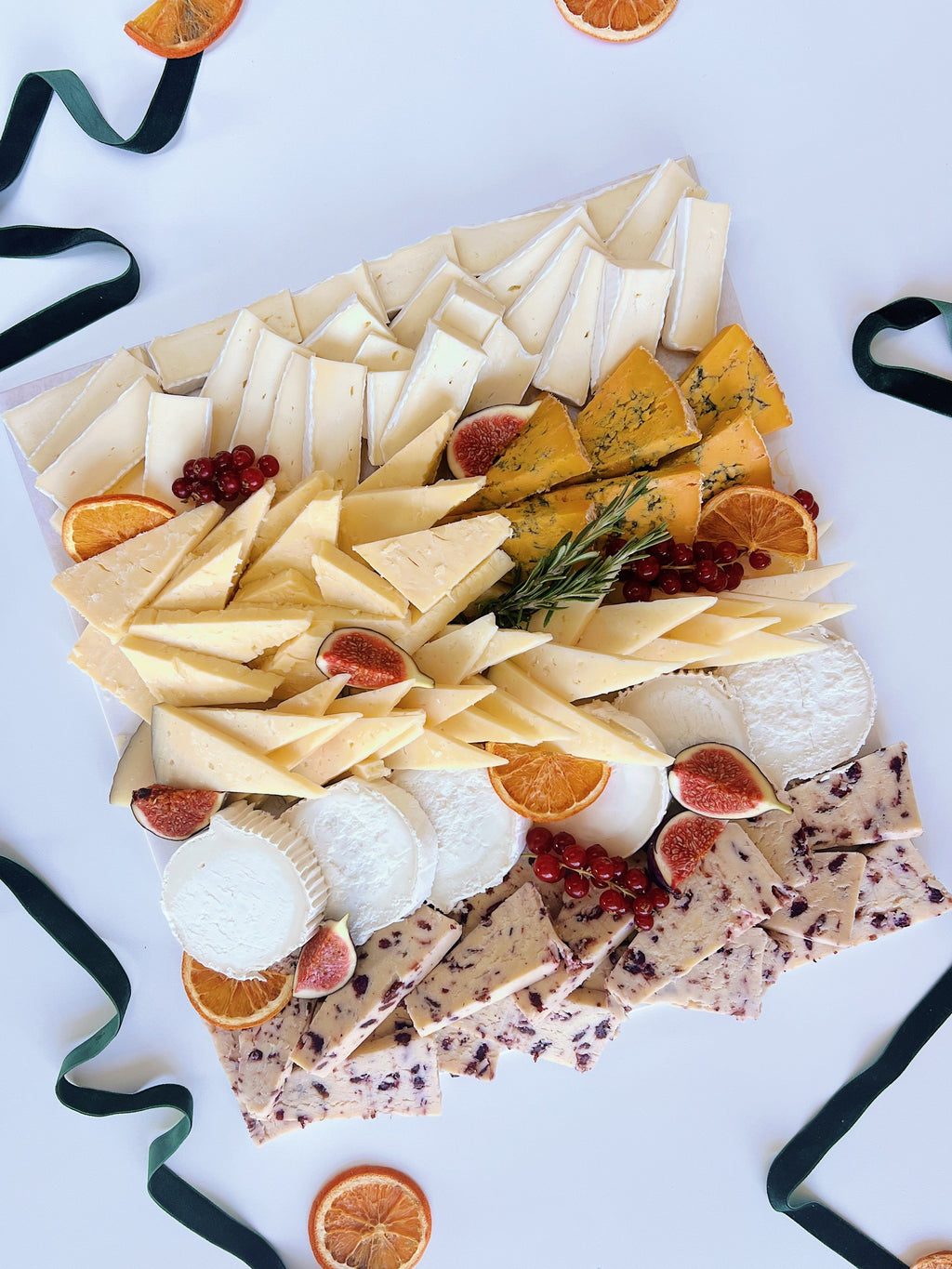 Assorted cheese platter with fruits and crackers on a white background