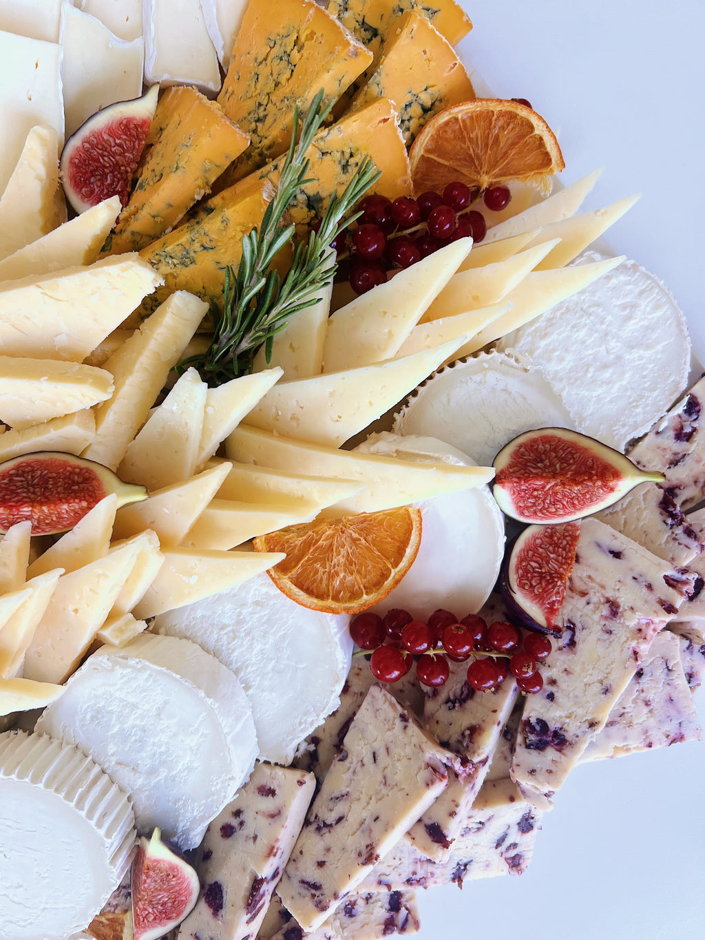 Assorted cheese platter with fruits and crackers on a white background